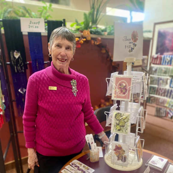 a woman in a pink sweater stands behind a table with cards and a display.