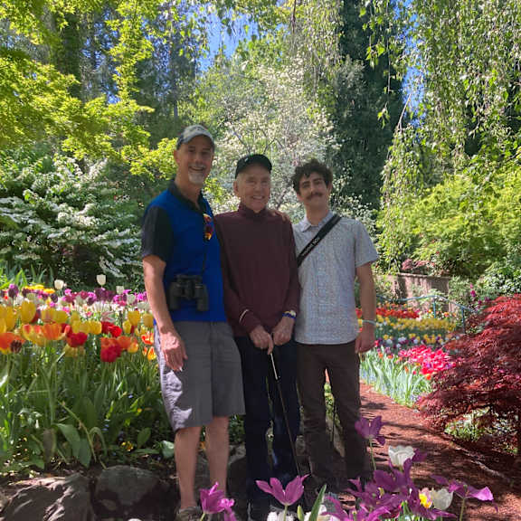 three men standing in a garden with flowers.