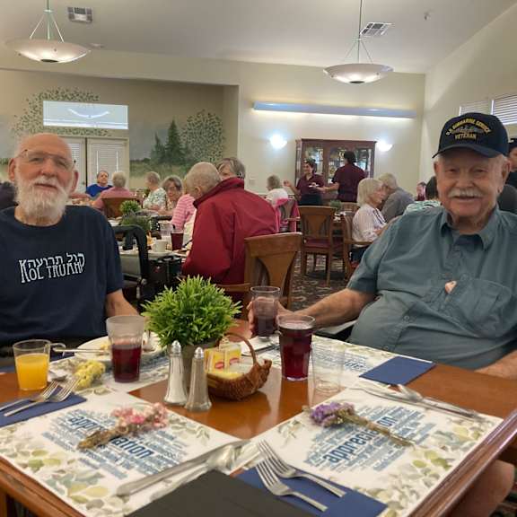 two men wearing caps sitting at a table with drinks and a menu.