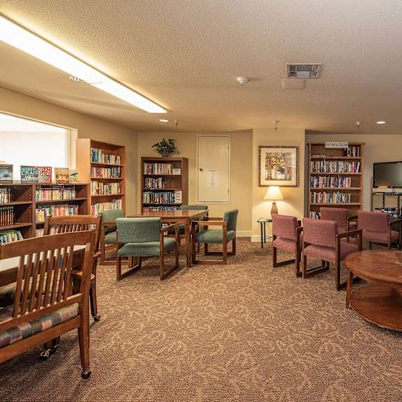 a library with tables and chairs and shelves of books at hilltop commons senior living, grass valley, ca