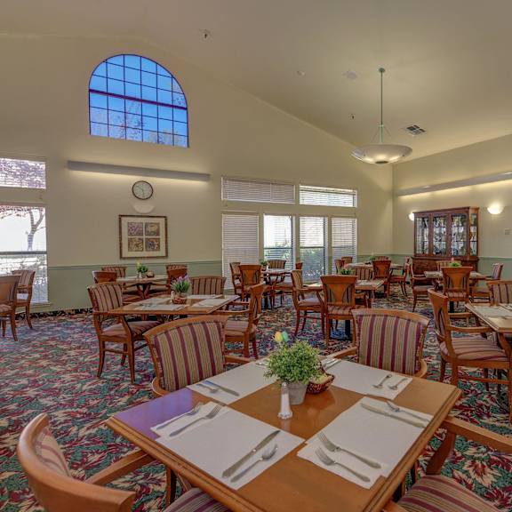 a dining room with tables and chairs and a large window at hilltop commons senior living, grass valley, ca