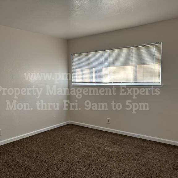 a room with a window covered by blinds and a door on the right side.