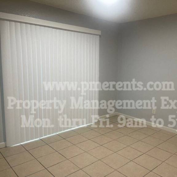 an empty living room with white blinds and a tiled floor
