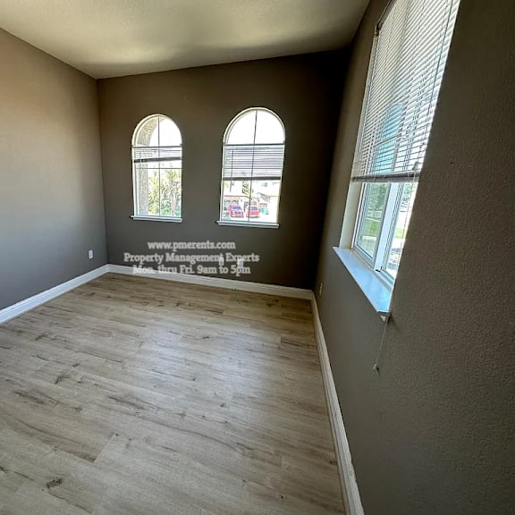 a room with wooden flooring and two arched windows.