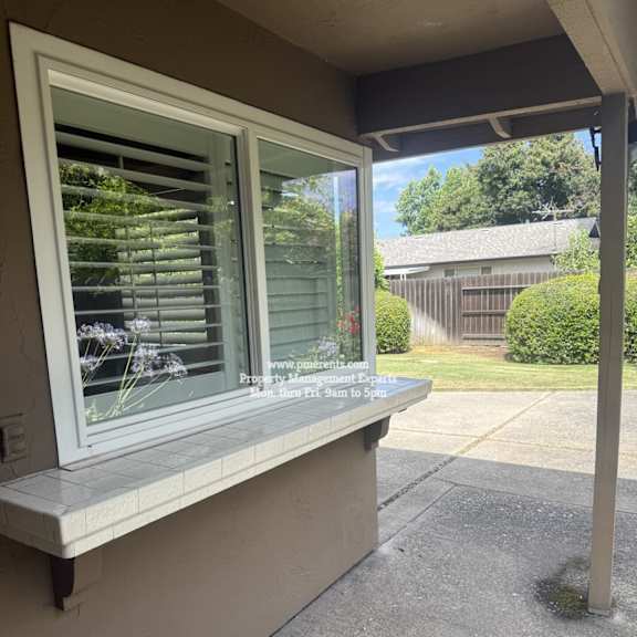 a window with blinds on a house with a view of a backyard.