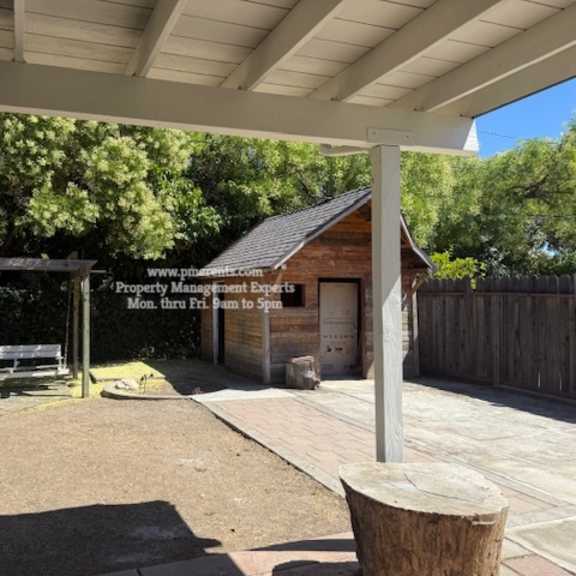 a small wooden building with a sign that reads "property management" is surrounded by a wooden fence and a bench under a canopy.