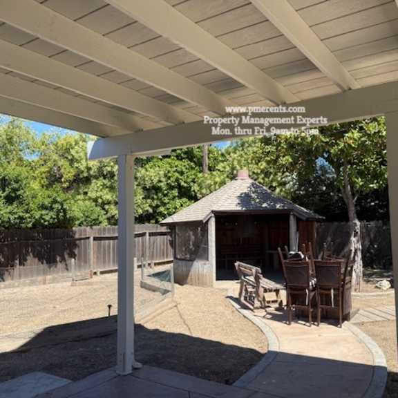 a gazebo is surrounded by a white pergola and a wooden fence.