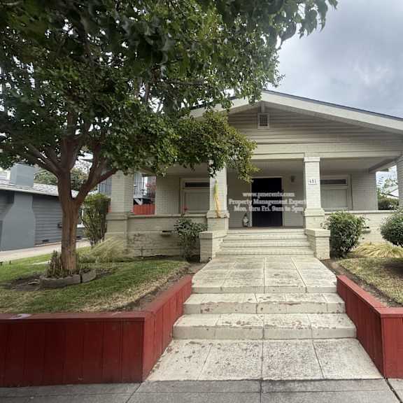 a white building with a porch and a tree in front.