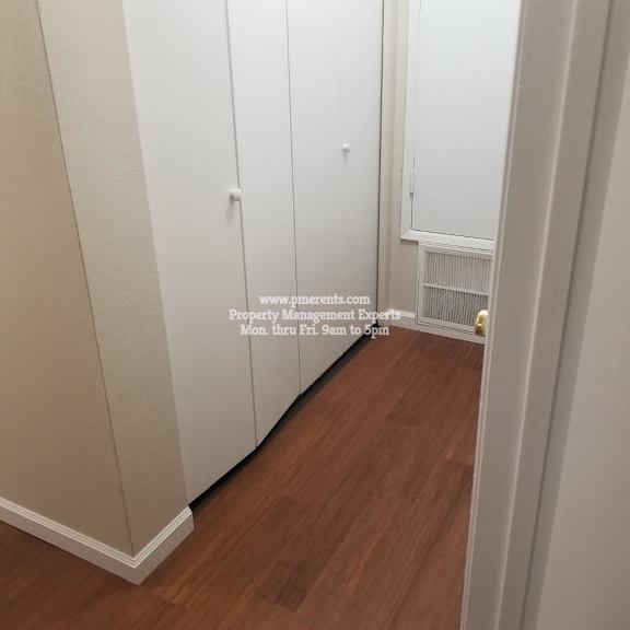 a hallway with wooden floors and white walls leading to a door.