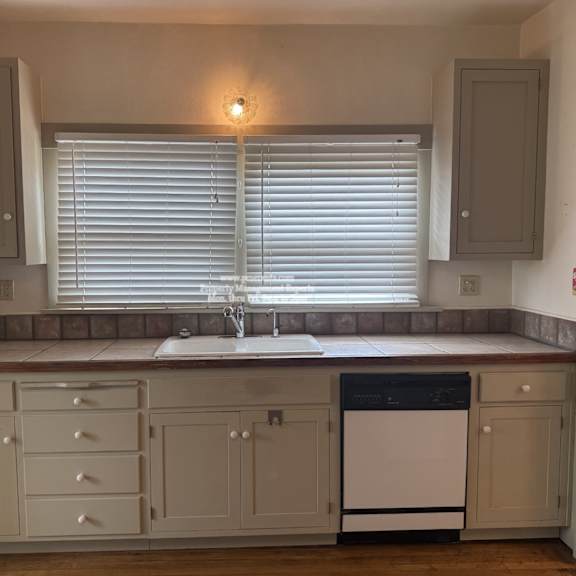a kitchen with a dishwasher and a window with blinds.