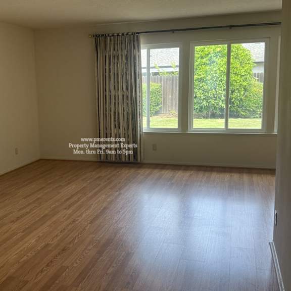 a room with wooden flooring and a window with a view of a fence and greenery.
