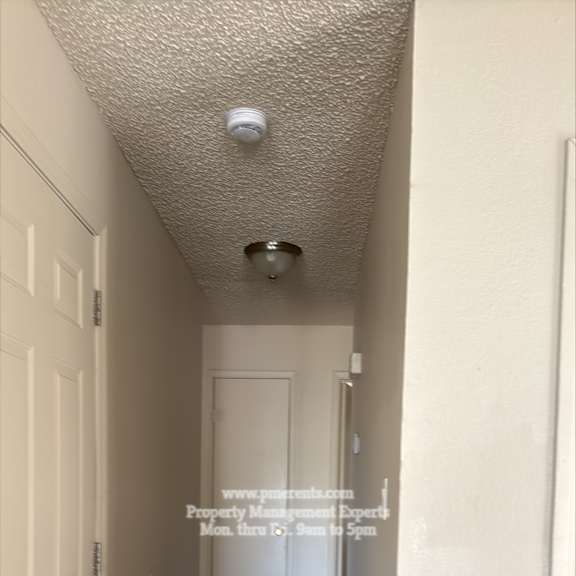 a long, narrow hallway with white doors and a light on the ceiling.