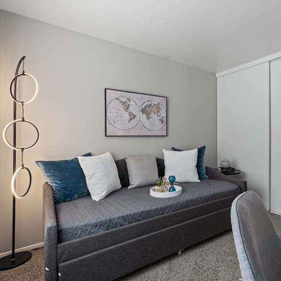 a modern bedroom with a grey bed, a grey chair, a white cabinet, and a framed world map on the wall.