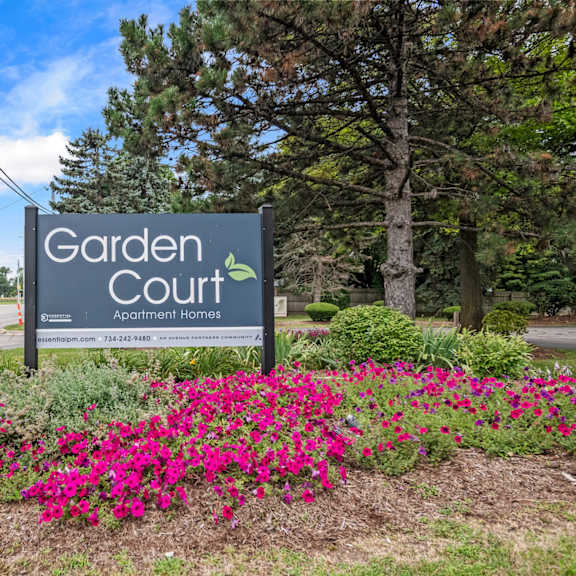 a sign for garden court apartments is surrounded by flowers.