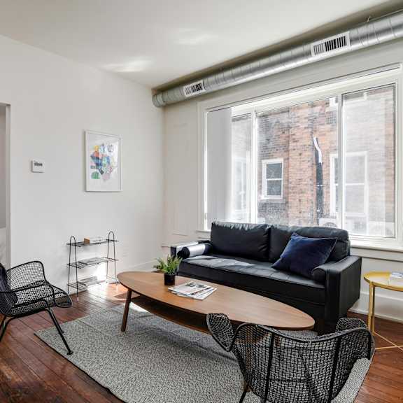 a living room with a black couch, a chair, a small table, and a window.