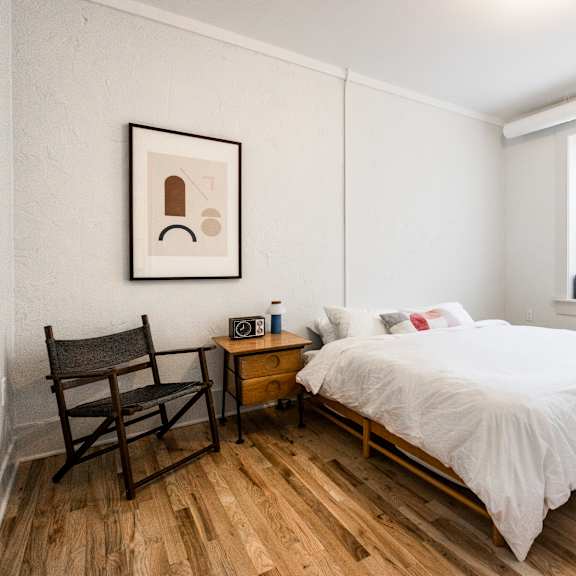 a bedroom with a bed, chair, and two pictures on the wall.