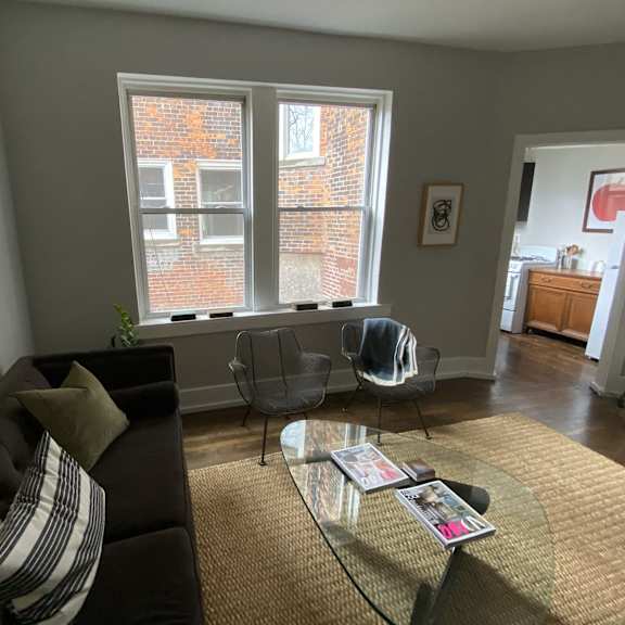 a living room with a couch and a glass coffee table and three windows