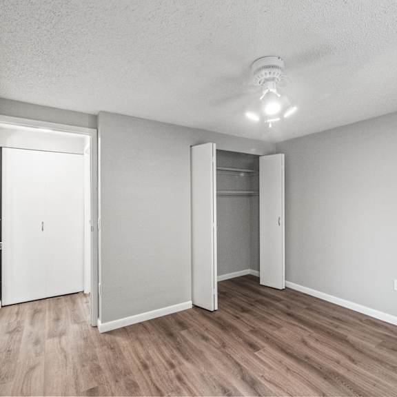 a room with a white ceiling, wooden floors, and white walls with a smoke detector on the ceiling.