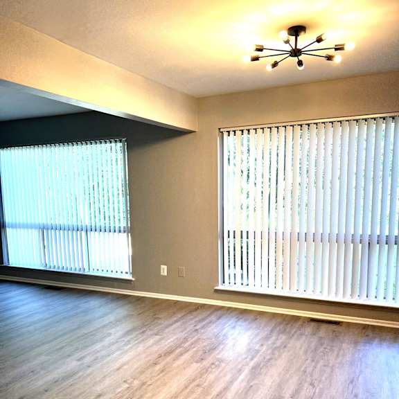 an empty living room with two windows and a chandelier