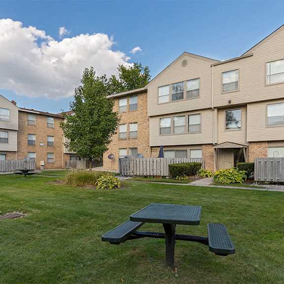 a green picnic table is in the foreground of a grassy area in front of apartment buildings.