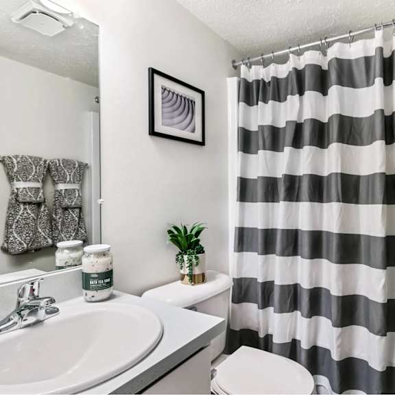 a bathroom with a striped shower curtain and a plant on the toilet.