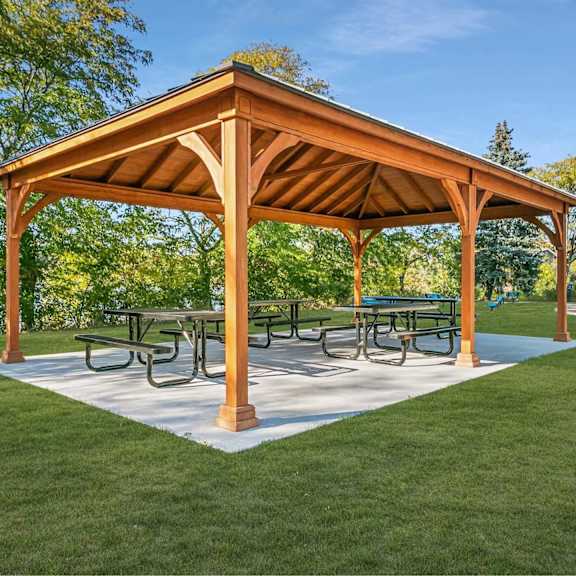 a wooden pavilion with a white base and a roof is surrounded by a grassy area.