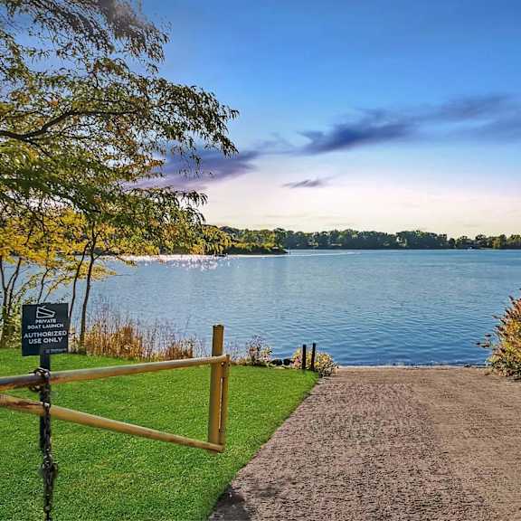 a pathway leads to a body of water with a sign on the left.