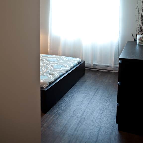 a bedroom with a bed, dresser, and window with curtains.