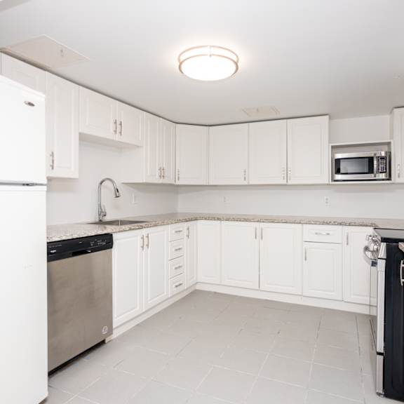 a white kitchen with a refrigerator on the left and a microwave on the right.