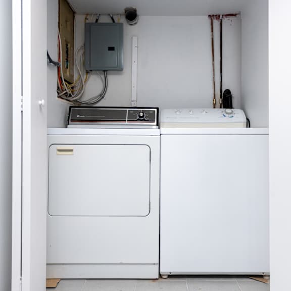 a white dryer is in a small room with a washing machine and a ventilation pipe.