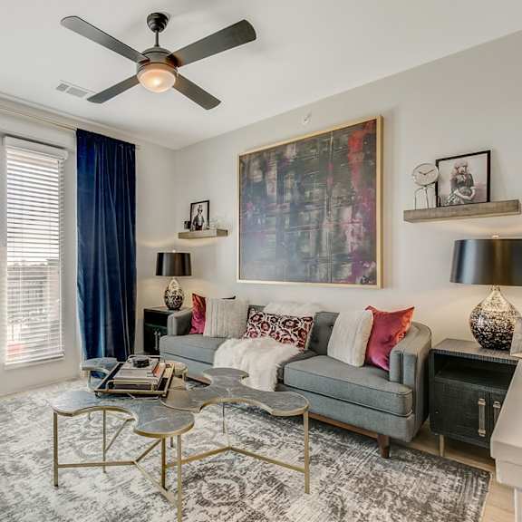 a living room with a grey couch, a coffee table, and a ceiling fan.