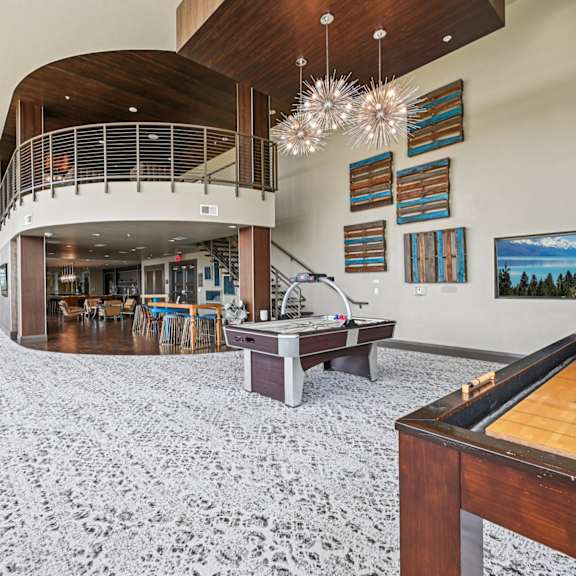 a billiard table is in the foreground of a spacious room with a staircase and a balcony.