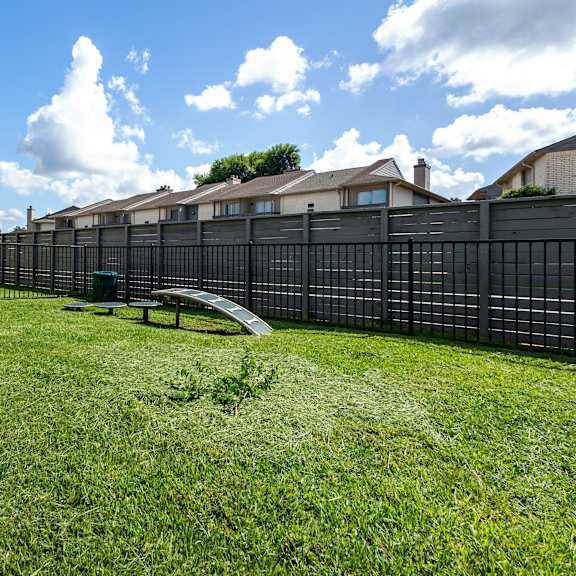 a black fence surrounds a green lawn with a bench and frisbees.