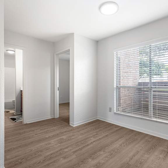 a room with a window covered by blinds and wooden flooring.