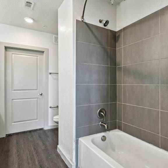 a modern bathroom with a white tub and grey tiles.
