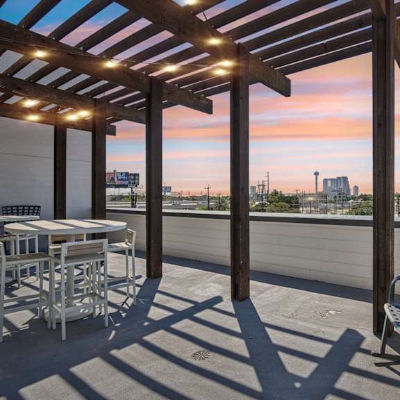 a patio with a table and chairs overlooking a city skyline at sunset.
