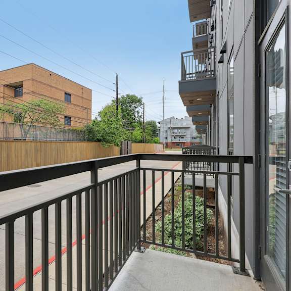 a balcony with a black railing overlooks a courtyard with a small garden.