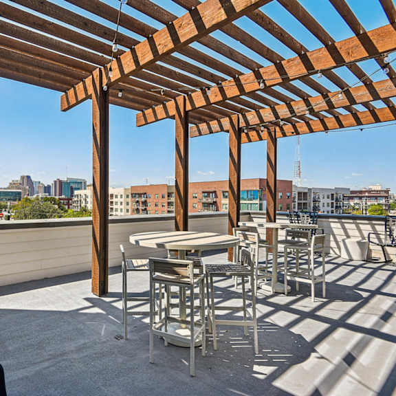 a wooden pergola over a table and chairs on a rooftop.