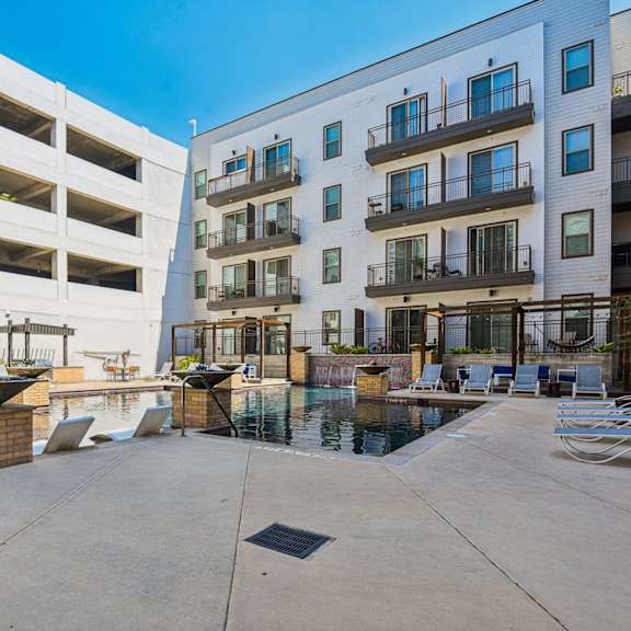 a sunny day at a modern apartment complex with a pool and lounge chairs.