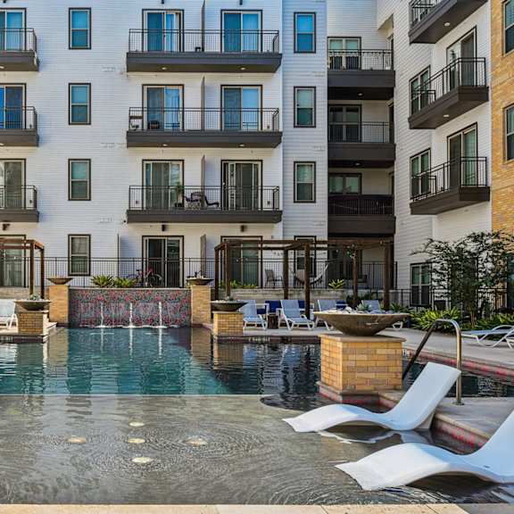 a pool surrounded by white lounge chairs in front of a building.