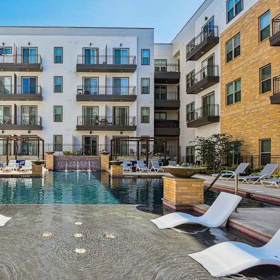 a pool surrounded by white lounge chairs and buildings with balconies.