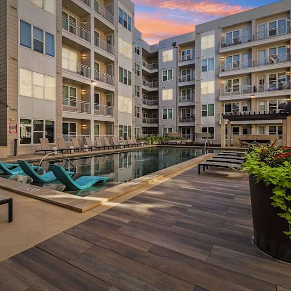 a pool surrounded by lounge chairs and apartment buildings.