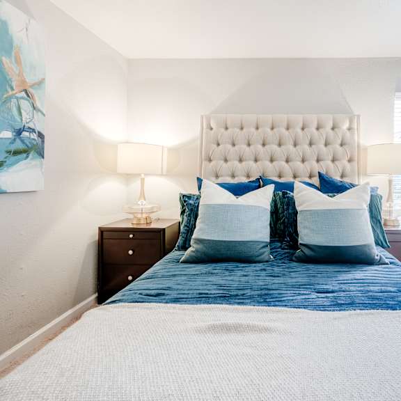 a bed with a white headboard and blue bedding sits in a room with white walls.