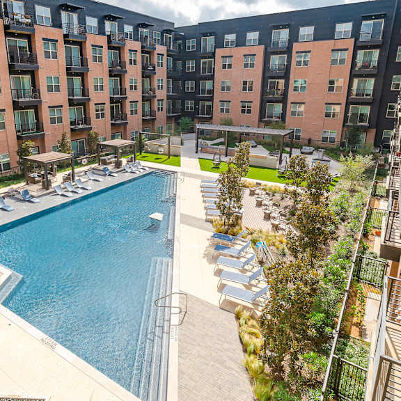 a large swimming pool surrounded by sun loungers and umbrellas in front of apartment buildings.