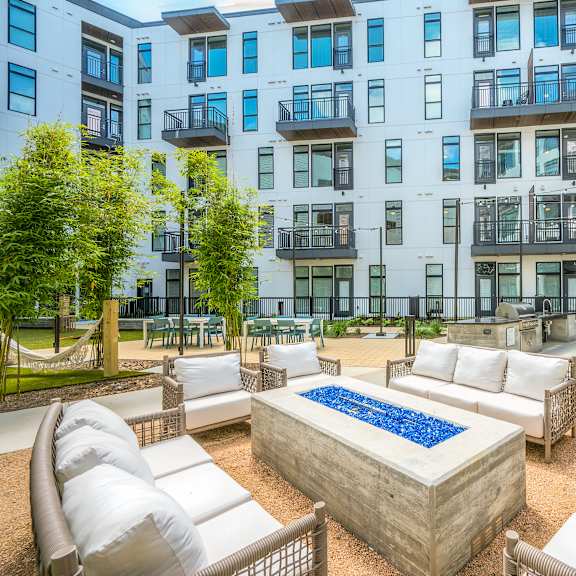 an outdoor lounge area with couches and a fire pit in front of an apartment building