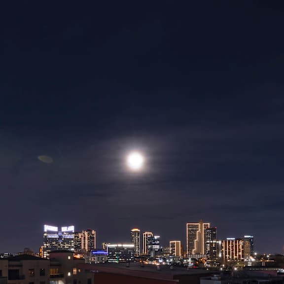 a cityscape at night with a bright moon in the sky.