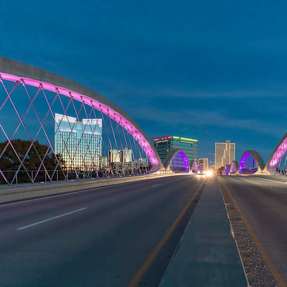a car is driving on a bridge with pink lighting.