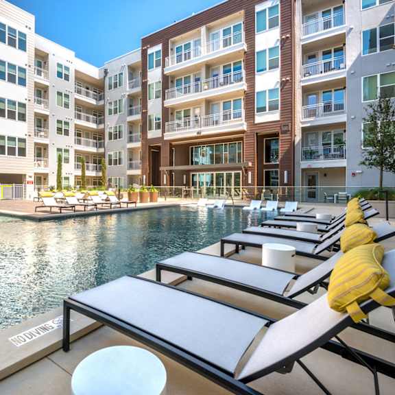 a pool area with lounge chairs and a building in the background.