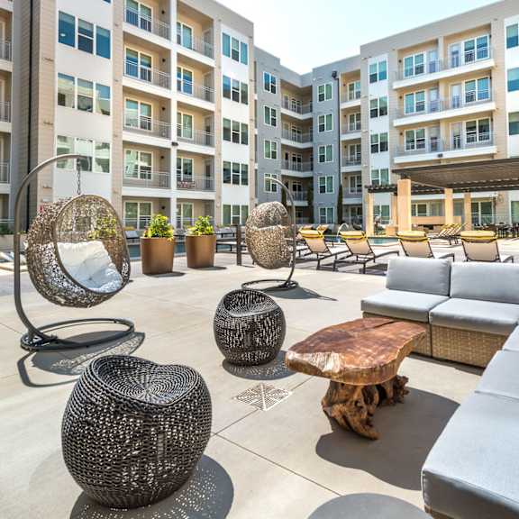 a large outdoor seating area with a variety of seating options including a circular woven chair and a wooden coffee table.