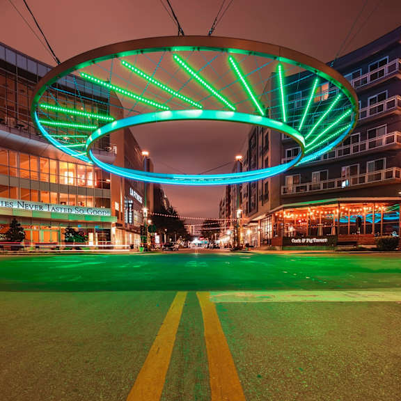 a neon sign in green and blue lights is above a street.